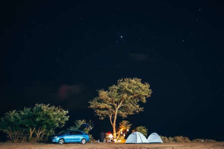 Group of five travellers rest on sea shore on evening sky background.