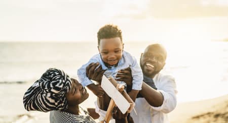 Happy African family having fun on the beach during summer vacation - Parents love and unity concept