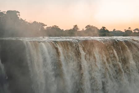Victoria Falls crest at sunrise with mist over Zambezi River gorge