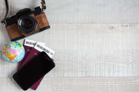travel and vacation concept - close up of passports, tickets, little globe, smart phone, vintage camera and copy space over wooden table background